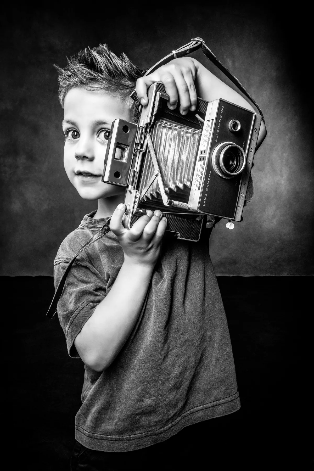 Young boy holding vintage camera during family portrait session at Richard Hill Studio in Dallas